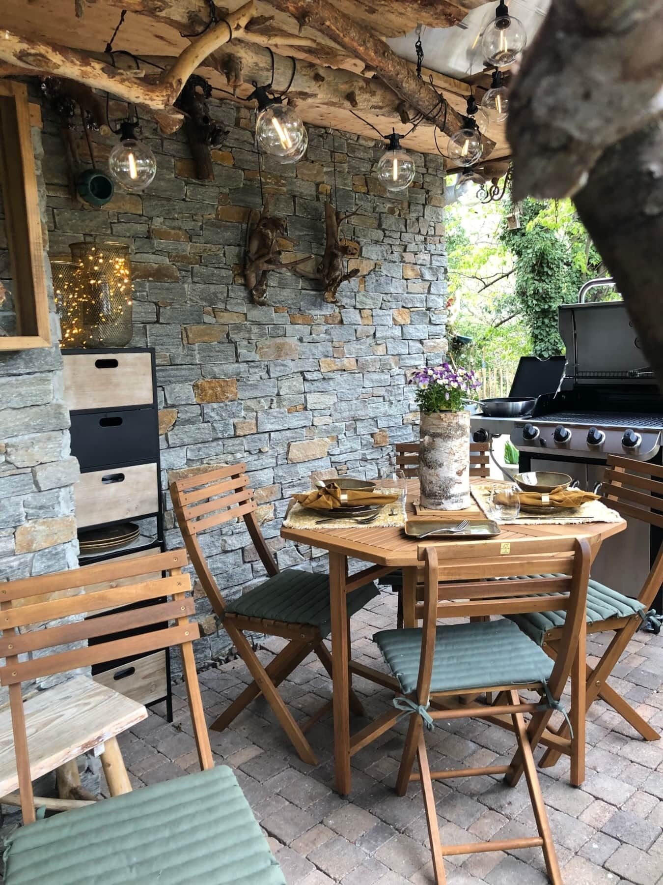 Ein Essbereich im Freien mit Steinmauern, Holzmöbeln und einem Grill.