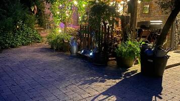 An outdoor patio area with brick flooring, potted plants, and a stone wall in the background.