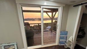 A room with a view of a sunset over a body of water, a sliding glass door, a blue chair, and a sign with family-oriented messages. - Lakeview Getaway with Stunning Sunsets with lake access (Newport)