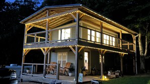 A two-story wooden cabin with a balcony, string lights, and a covered porch area. - Lakeview Getaway with Stunning Sunsets with lake access (Newport)
