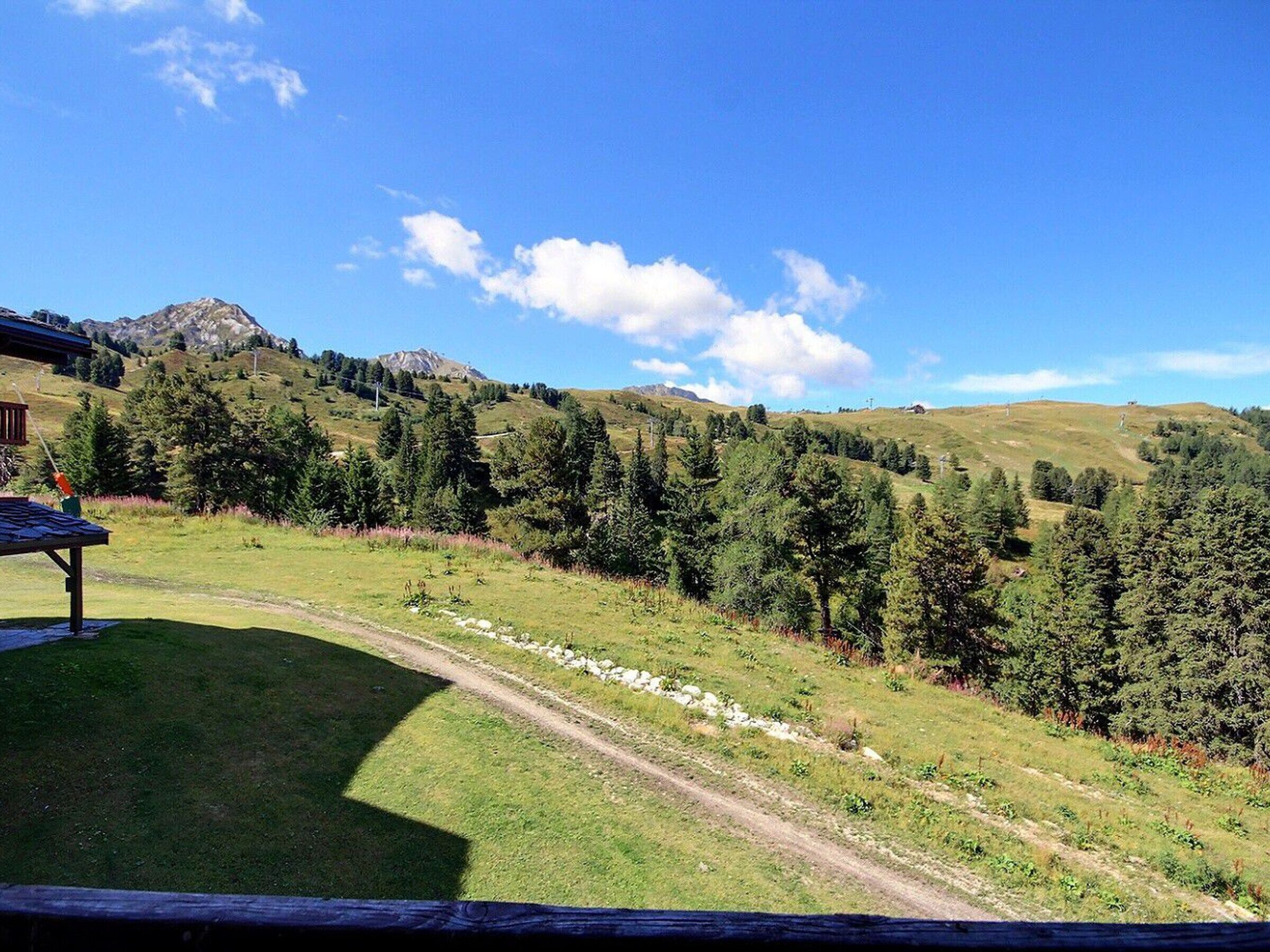 A scenic view of a mountain landscape with a clear sky, a dirt path, and a wooden structure.