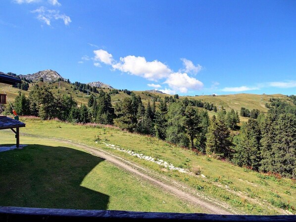 A scenic view of a mountain landscape with a clear sky, a dirt path, and a wooden structure.
