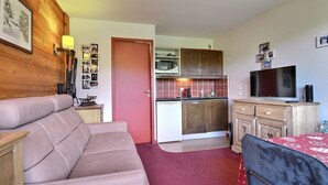 Ett kompakt bostadsutrymme med en soffa, ett litet kök och en tv.