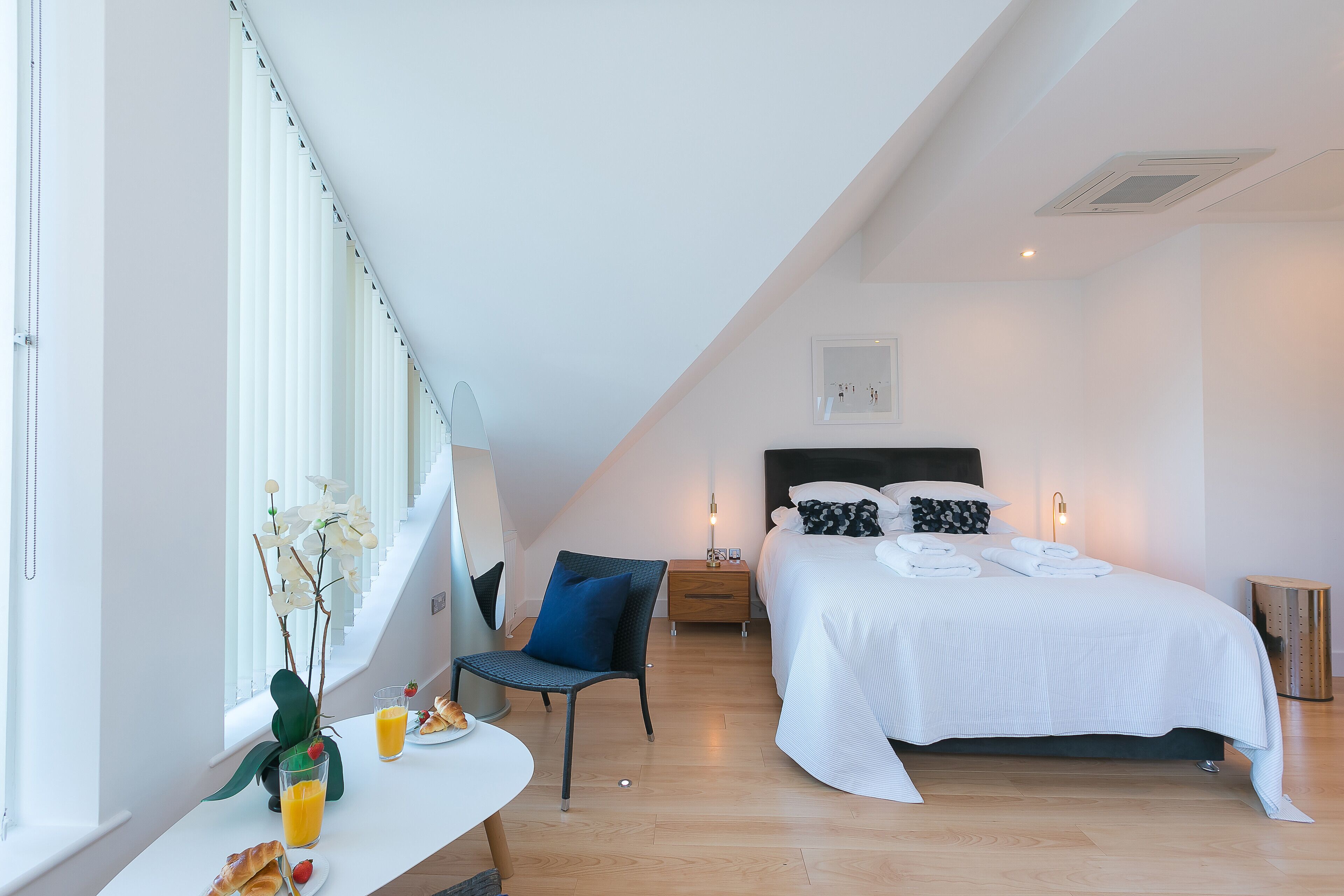 Une chambre moderne avec un lit, des tables de chevet, une chaise et une table à manger où sont disposés des aliments pour le petit-déjeuner.