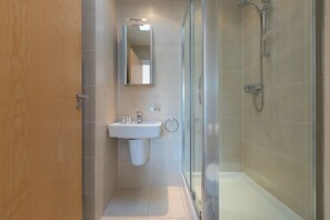 A modern bathroom with a glass shower enclosure, a sink with a mirror above it, and a wooden door.