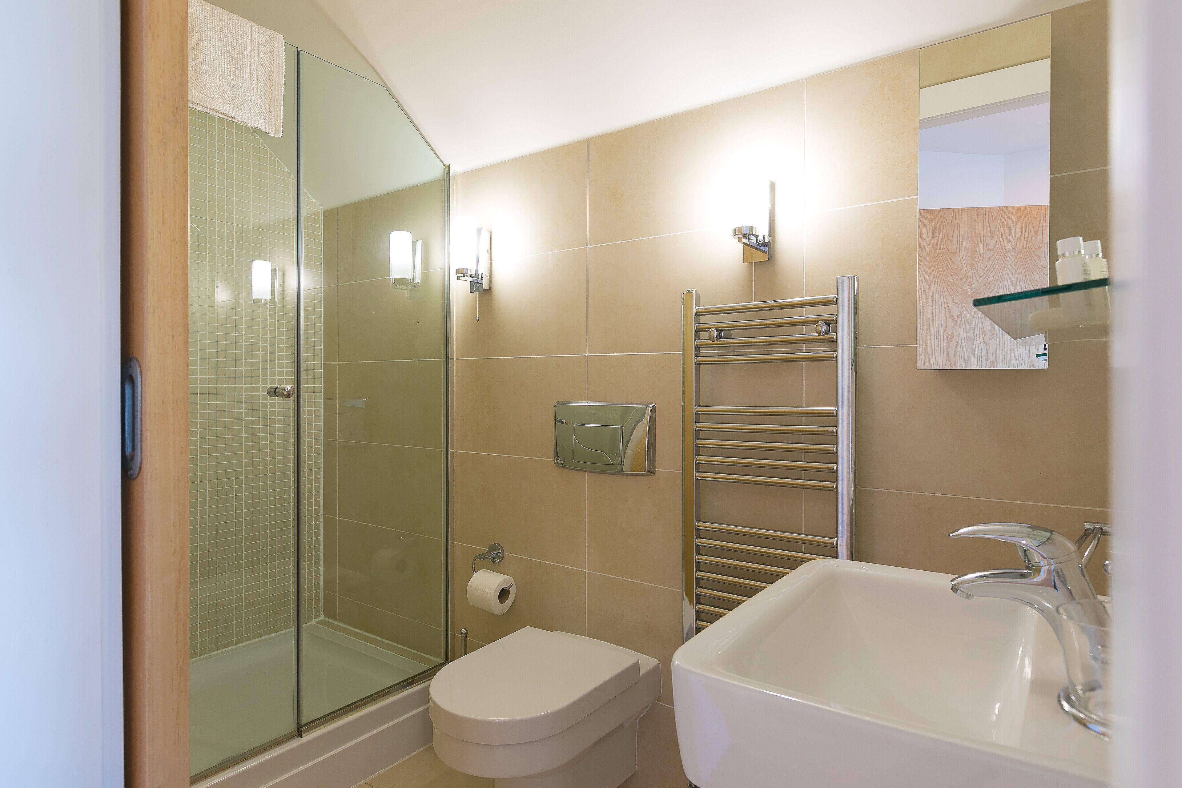 Un baño con cabina de ducha de vidrio, inodoro, lavabo con espejo y toallero.
