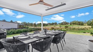 An outdoor patio with a dining table set for six, surrounded by chairs, under a covered area with a ceiling fan.