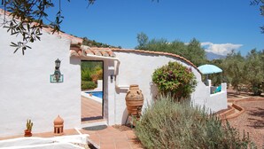 A white building with a tiled roof, a visible door, and a small garden area with a potted plant and a large terracotta pot. - Romantic and private hide away with pool in Andalusia. (Comares)