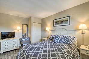 Une chambre à coucher comprenant un lit, une télévision, une commode, une chaise et deux tables de chevet avec des lampes.