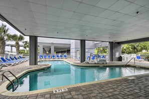 Une piscine entourée de chaises longues bleues, d’une terrasse carrelée et d’un espace abrité avec des piliers.