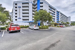 Un hôtel à plusieurs étages aux couleurs bleu et blanc, avec un pilier central bleu, des places de stationnement et un espace paysager agrémenté d’arbres.