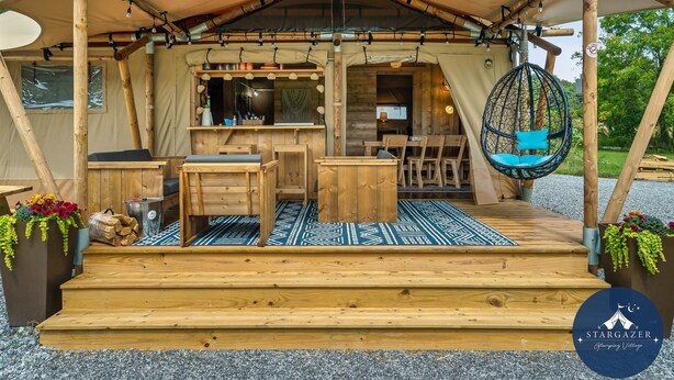 Une tente en bois comprenant un espace cuisine, des sièges et un fauteuil suspendu.