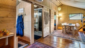 Un intérieur en bois comprenant un coin repas, un porte-manteau et une porte coulissante donnant accès à une salle de bain.
