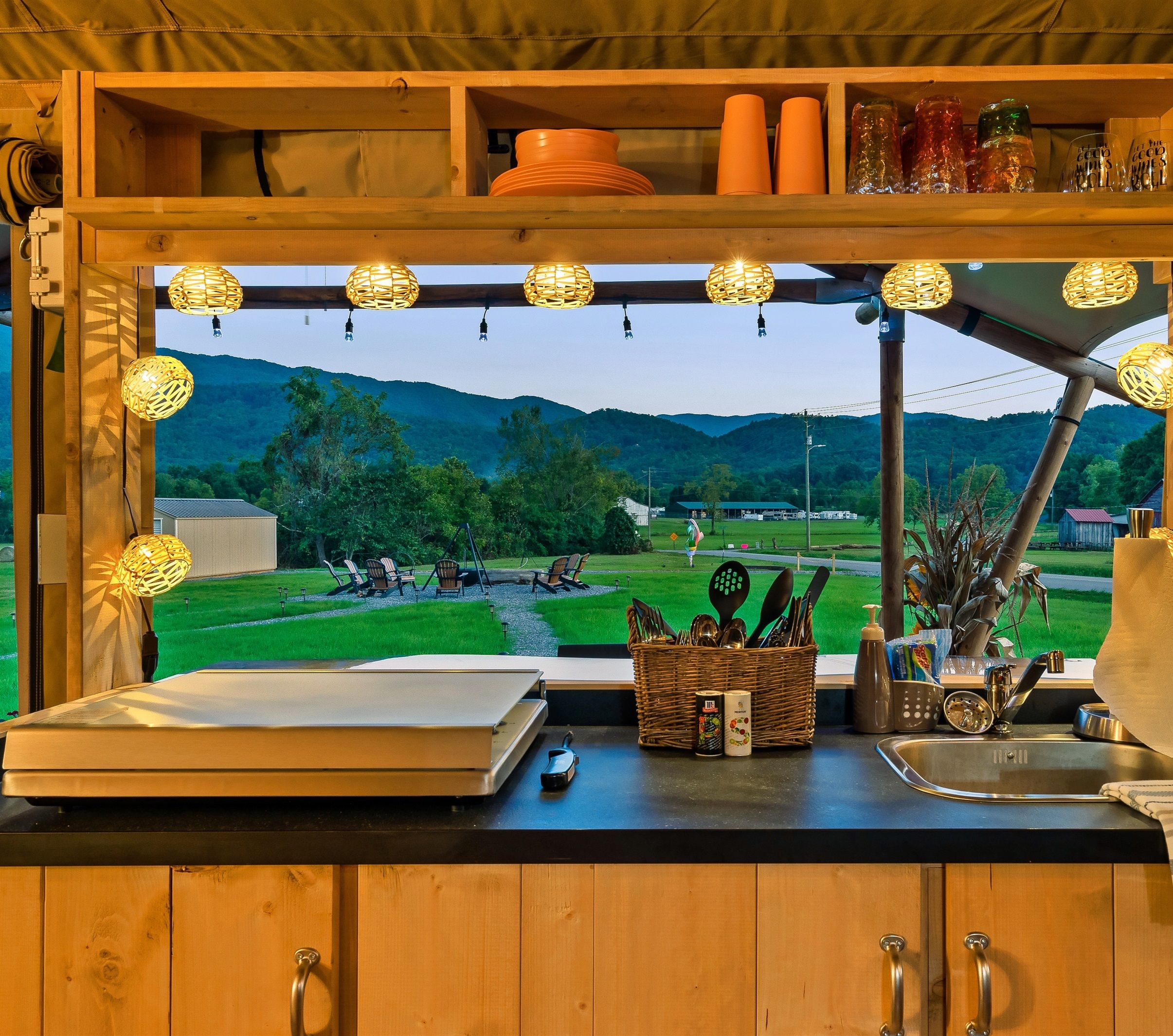 A kitchen with a large window overlooking a scenic landscape, wooden cabinets, and various kitchen utensils.