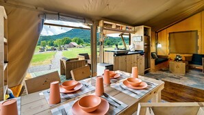 Alojamiento en carpa con comedor dispuesto para los huéspedes, con una mesa con platos y cuencos anaranjados, mobiliario de madera y vistas del paisaje circundante.