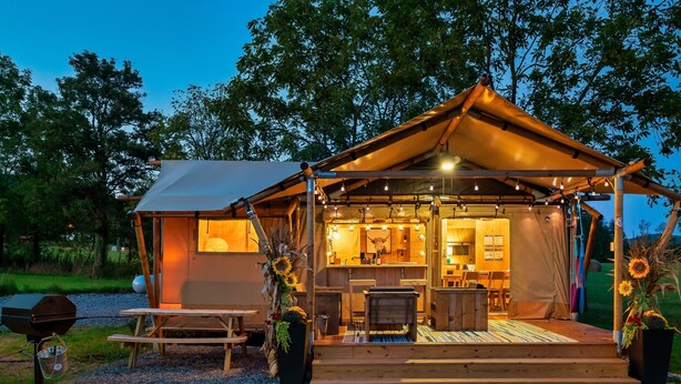 Un acogedor camping de lujo con una estructura de madera, un comedor y una parrilla.