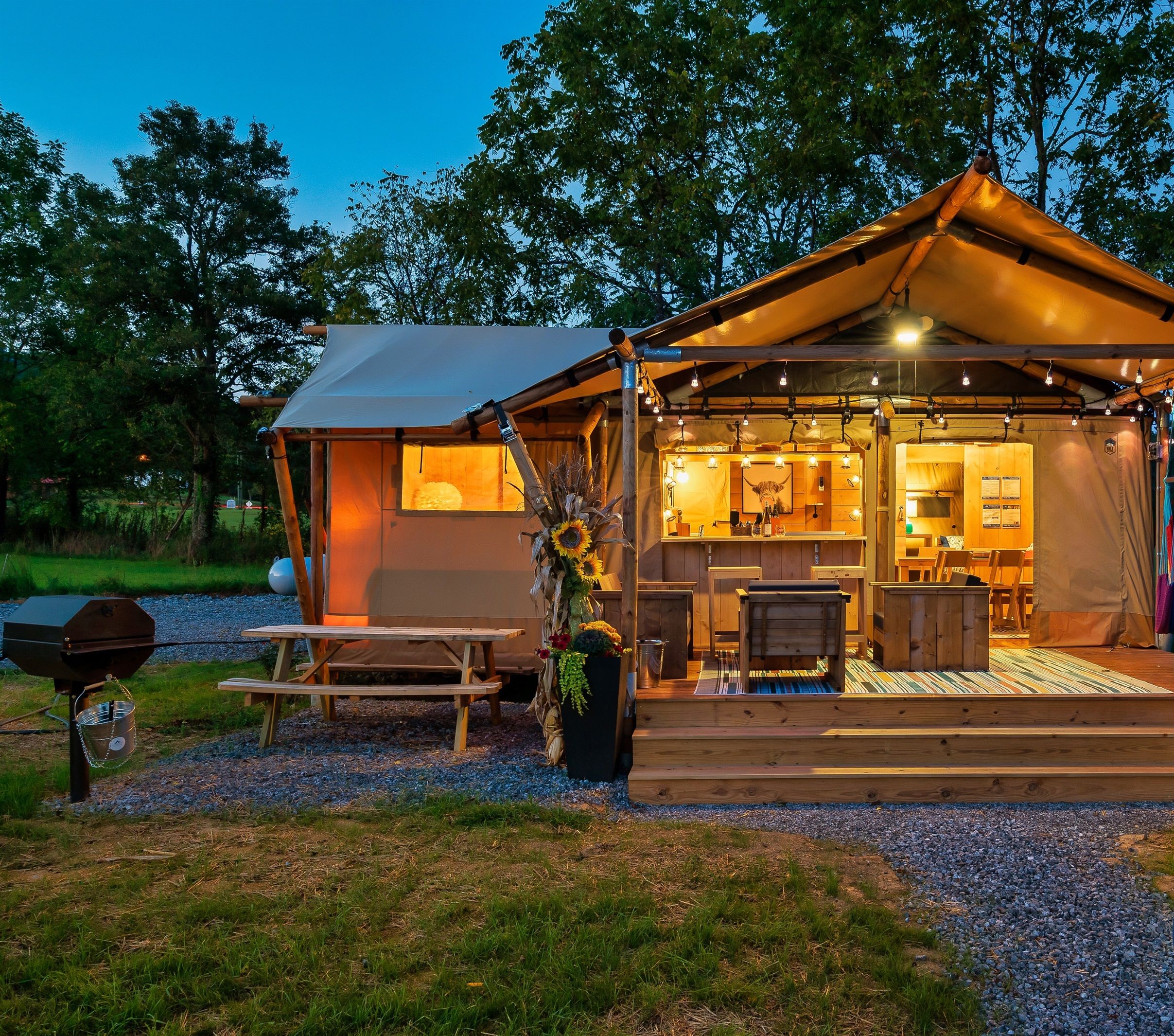 Een sfeervol kampeerterrein met een houten constructie, een eethoek en een barbecue.