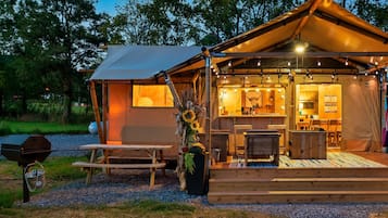 Een sfeervol kampeerterrein met een houten constructie, een eethoek en een barbecue.