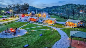 Um camping com várias cabanas, uma área de refeições central e uma fogueira.