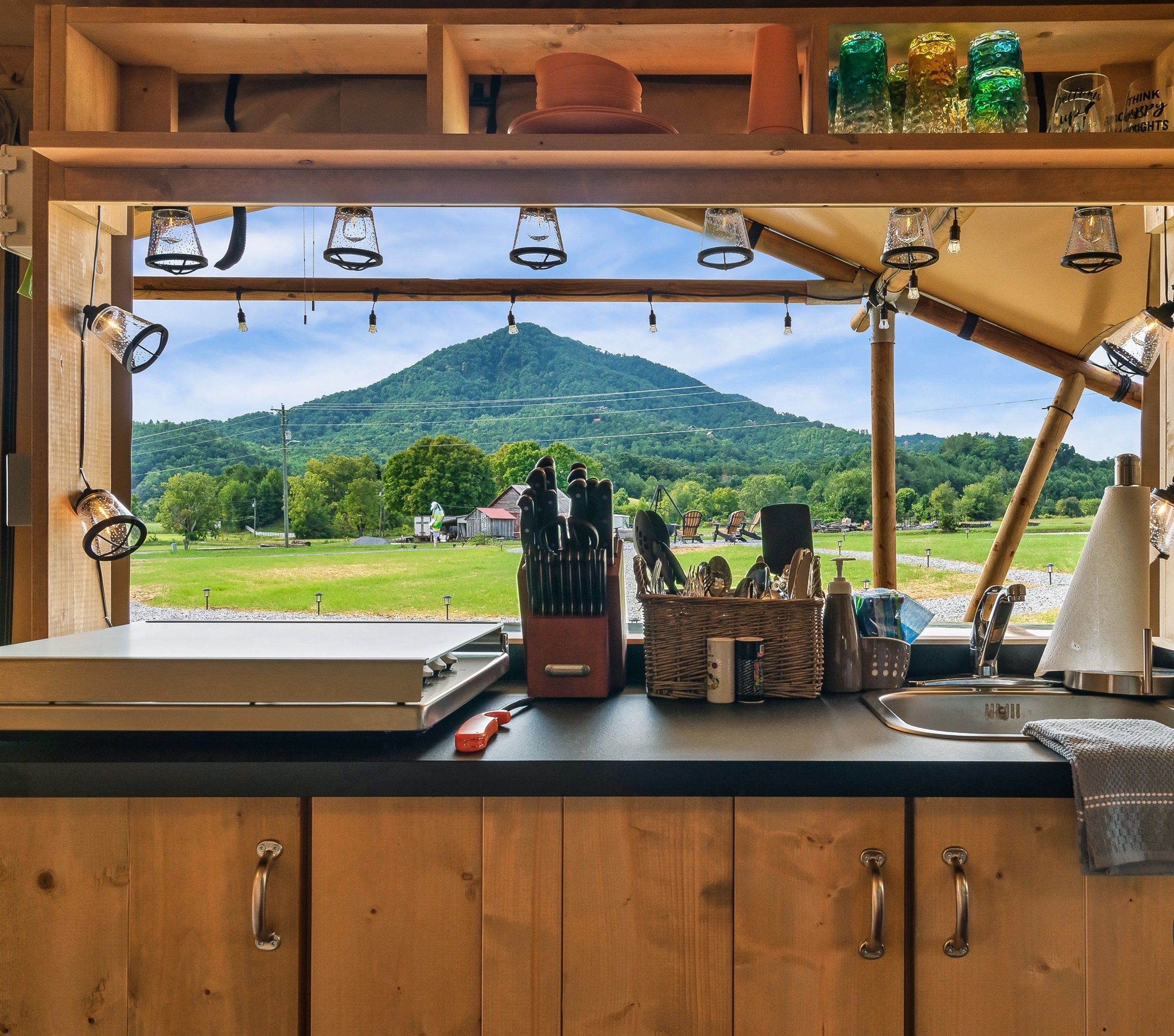 A kitchen with a view of a mountain, wooden cabinets, a sink, and various utensils.