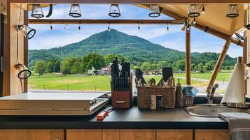 A kitchen with a view of a mountain, wooden cabinets, a sink, and various utensils.