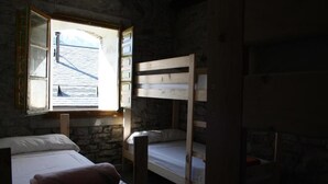 A room with bunk beds, a stone wall, and a window with an open shutter. - Encantaria SLU (Broto)