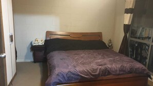 Ein Schlafzimmer mit einem hölzernen Bett, einem Nachttisch, einem kleinen Tisch mit Lampe und einem Fenster mit Vorhängen.