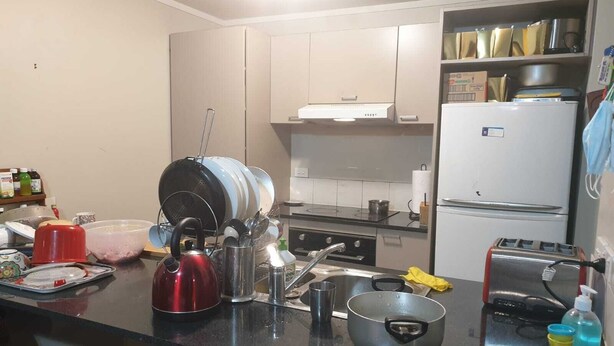 Eine Küche mit Herd, Spüle und Kühlschrank. Auf der Arbeitsfläche befinden sich verschiedene Küchenutensilien, darunter ein Wasserkocher, Töpfe und ein Toaster.