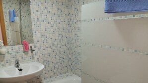Un baño con un lavabo blanco, cabina de ducha con mampara de vidrio y pared revestida con azulejos.