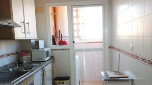 Una cocina compacta con armarios blancos, un microondas, un lavabo y un pequeño cubo de basura.