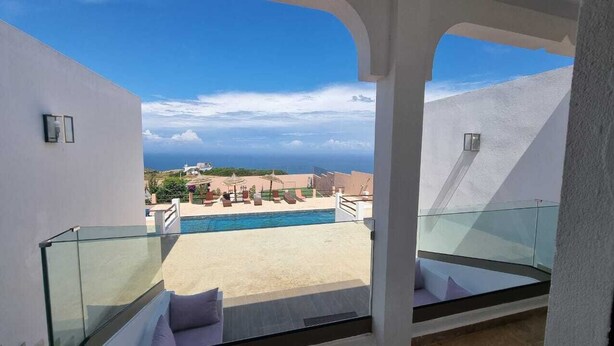 Un balcón con baranda de vidrio que da a una piscina y un cielo despejado.