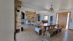 Amplia sala de estar con pared de piedra, mesa de madera con bancos y un sofá con cojines.