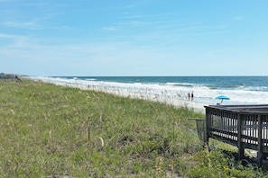 Une plage avec une promenade en bois et un parasol bleu.