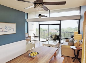 Une pièce spacieuse avec une grande fenêtre, un ventilateur de plafond, une table à manger ornée d’un saladier rempli de citrons et un canapé.