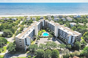 Un hotel de varios pisos con un patio central que cuenta con una piscina, rodeado de exuberante vegetación y vistas a la playa.