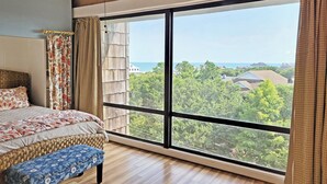 A bedroom with a large window, a bed, a bench, and a ceiling fan.
