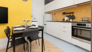 A modern kitchen with white cabinets, a black countertop, and a yellow backsplash. There is a dining table set with plates and glasses.