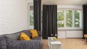 A modern living room with a grey sofa, yellow cushions, a white coffee table, and a window with black curtains.