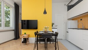 A modern kitchen with a yellow accent wall, a dining area with a black table and chairs, and a TV mounted above the table.