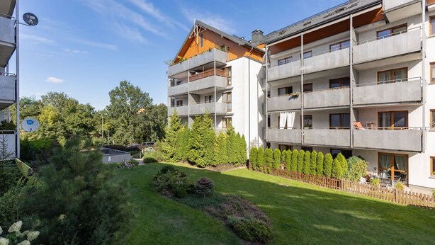 A multi-story residential building with balconies, a well-maintained lawn, and surrounding greenery.