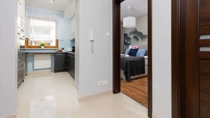 A modern hotel room with a wooden floor, a bed with a dark bedspread, a white wall, and a window with sheer curtains.