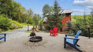 A rustic cabin with a fire pit and Adirondack chairs in a forested area.