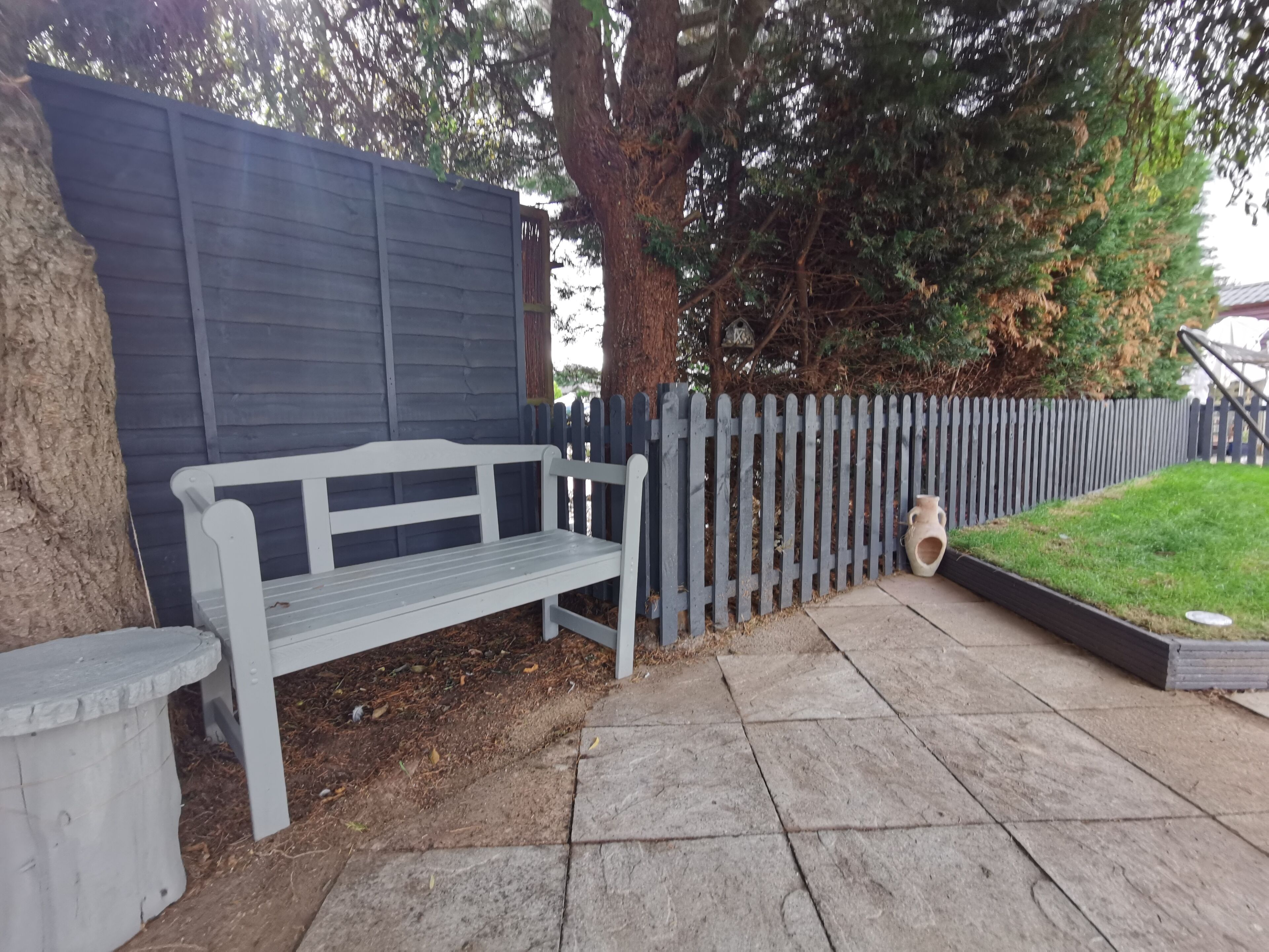 Un banco y una pequeña mesa en un jardín con cerca de madera y un árbol.