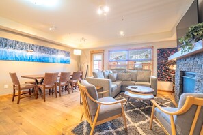 A living room with a sofa, chairs, a coffee table, a fireplace, and a dining area with a table and chairs. - Luxe Condo with Mountain Views, Balcony & BBQ (Canmore)