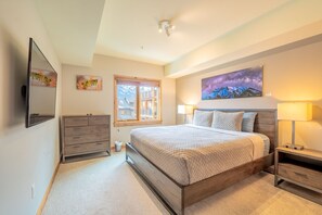 A bedroom with a bed, bedside tables, a dresser, a window, and a painting on the wall. - Luxe Condo with Mountain Views, Balcony & BBQ (Canmore)