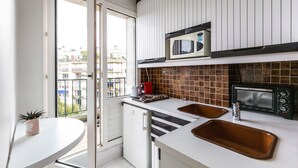 Uma cozinha compacta com bancada branca, duas pias, micro-ondas e forno tostador.