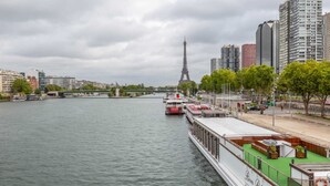 Um rio com barcos, uma ponte e a Torre Eiffel ao fundo.