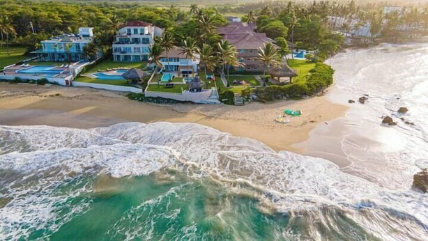 Propiedad frente al mar con varias edificaciones, piscina y palmeras.