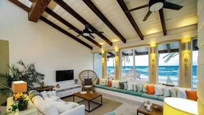 Amplia sala de estar con un gran ventanal con vistas al océano, un ventilador de techo y un conjunto de asientos cómodo.