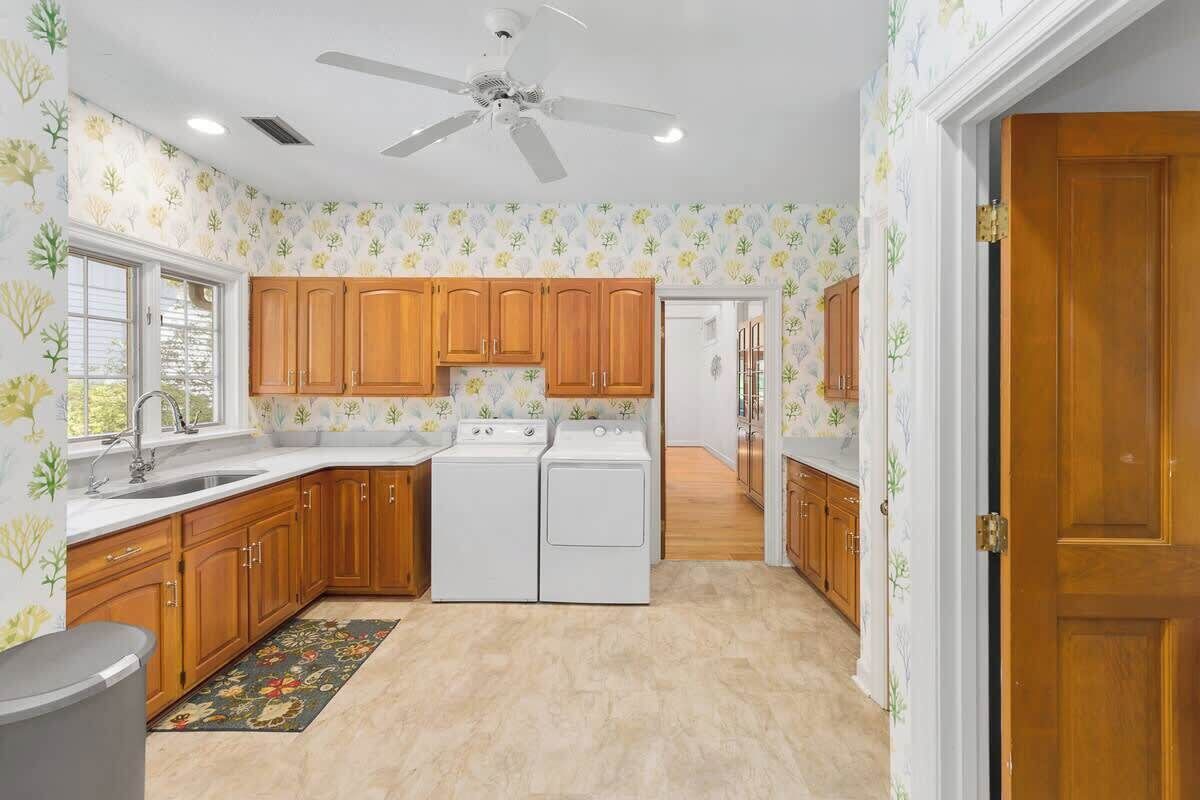 A kitchen with wooden cabinets, a double sink, a ceiling fan, and a patterned rug.